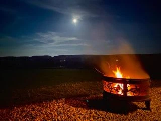 Outdoor firepit burning at night beneath a clear sky illuminated by a full moon.