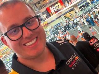Man taking a selfie in front of a Formula 1 pit stop.